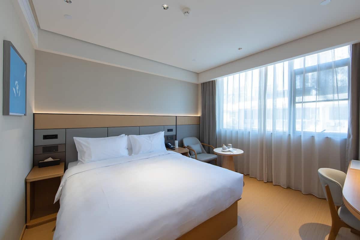 A hotel room with a large bed, bedside tables, a desk, and a chair.