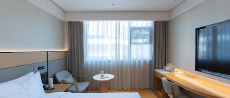 A hotel room with a bed, a desk, a chair, a small table, and a TV.