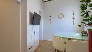 Uma zona de refeições moderna com mesa de vidro, duas cadeiras, televisão de ecrã plano na parede e decorações nas paredes.
