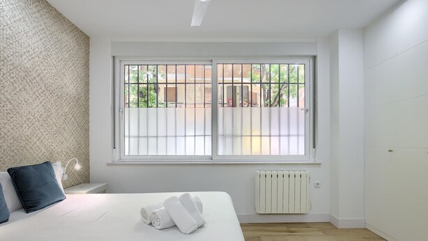 Una camera da letto con un letto grande, una finestra con inferriate, un termosifone e una ventola a soffitto.