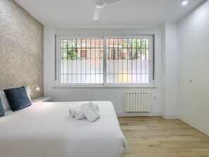 A bedroom with a large bed, a window with metal bars, a radiator, and a ceiling fan.