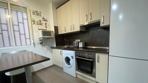 A compact kitchen with a washing machine, oven, and microwave. - Madrid Ferrocarril - 2-Bedroom Apartment (Madrid)