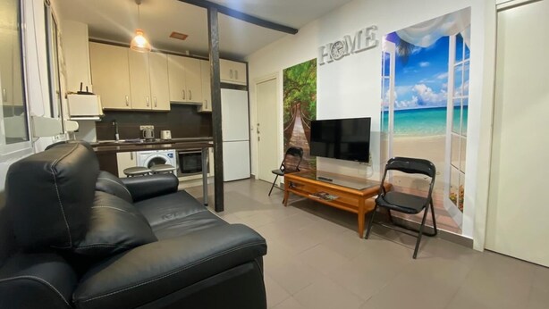 A compact living space with a sofa, a TV, and a kitchen area. - Madrid Ferrocarril - 2-Bedroom Apartment (Madrid)
