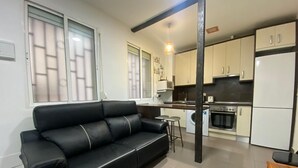 A modern apartment with a black leather sofa, a kitchen with white cabinets, and a dining area with a small table and stools. - Madrid Ferrocarril - 2-Bedroom Apartment (Madrid)