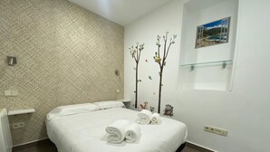 A neatly made bed with folded towels, a patterned wall, a small shelf with a decorative item, and a framed picture on the wall. - Madrid Ferrocarril - 2-Bedroom Apartment (Madrid)