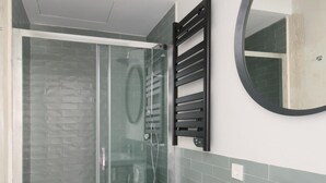 Een moderne badkamer met een douchecabine van glas, een witte wastafel en een zwarte handdoekhouder.
