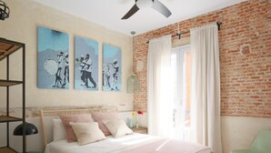 Een slaapkamer met een bakstenen muur, een bed met houten frame, een groene stoel en kunst aan de muur.