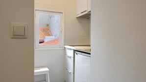 Una cocina compacta con armarios blancos, una pequeña ventana y un taburete blanco.