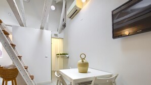 Una habitación moderna con decoración blanca, una mesa de comedor y sillas, una escalera blanca y un televisor montado.
