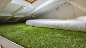 Dormitorio tipo loft con tragaluz, suelo de césped artificial verde y cama blanca.