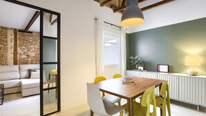 A modern dining area with a wooden table, yellow and white chairs, a hanging pendant light, and a brick wall in the background. - Madrid Serrano - Two-bedroom Apartment (Madrid)