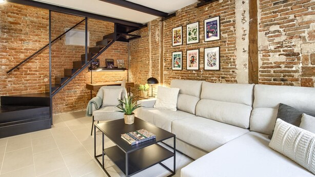 A modern living room with a brick wall, a staircase, a sofa, a coffee table, and a bookshelf. - Madrid Serrano - Two-bedroom Apartment (Madrid)