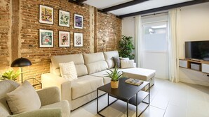 A living room with a brick wall, a sofa, a coffee table, and a TV. - Madrid Serrano - Two-bedroom Apartment (Madrid)