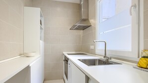 A compact kitchen with white cabinetry, a stainless steel sink, and a built-in oven. - Madrid Serrano - Two-bedroom Apartment (Madrid)