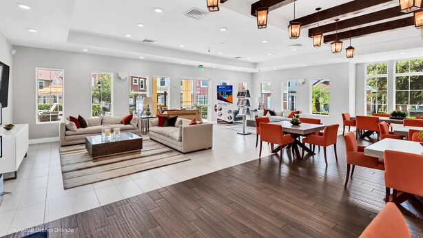 A spacious living area with a sofa set, a coffee table, and a dining area with orange chairs and white tables.