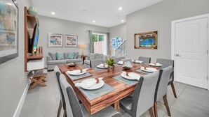 A modern dining area with a wooden table set for four, grey upholstered chairs, and a grey sofa in the background.