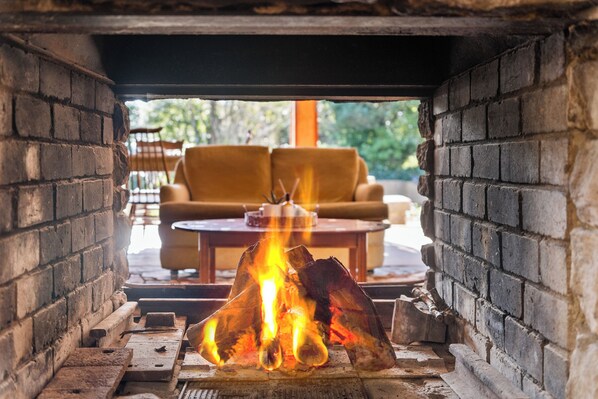 A fireplace with logs burning, a sofa, and a table in the background.