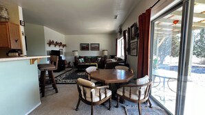 A dining area with a wooden table and chairs, a kitchen area with cabinets and a countertop, and a large window with curtains. - Javelina House - Lake Montezuma (Lake Montezuma)