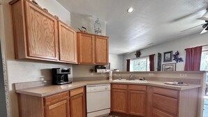 A kitchen with wooden cabinets, a coffee maker, a dishwasher, and a window with curtains. - Javelina House - Lake Montezuma (Lake Montezuma)