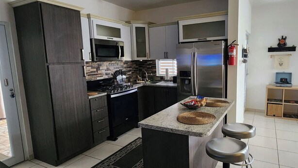 A modern kitchen with dark cabinetry, stainless steel appliances, and a central island with stools.