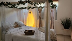 A bedroom with a bed, a bedside table, a basket, and a potted plant.