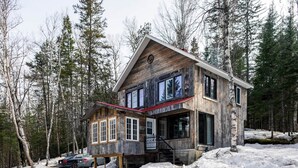 Une cabane en bois avec un toit rouge, de grandes fenêtres et un escalier menant à l’entrée.