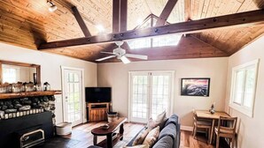 A cozy living room with a fireplace, a black sofa, a television, and a ceiling fan. - The Nest: Serene Sanctuary w Hot Tub, Fireplace, Grill, Hammock, Outdoor Fire Fe (Idyllwild-Pine Cove)