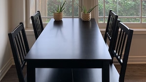 Un comedor con una mesa de madera oscura, cuatro sillas, dos macetas y una lámpara colgante.