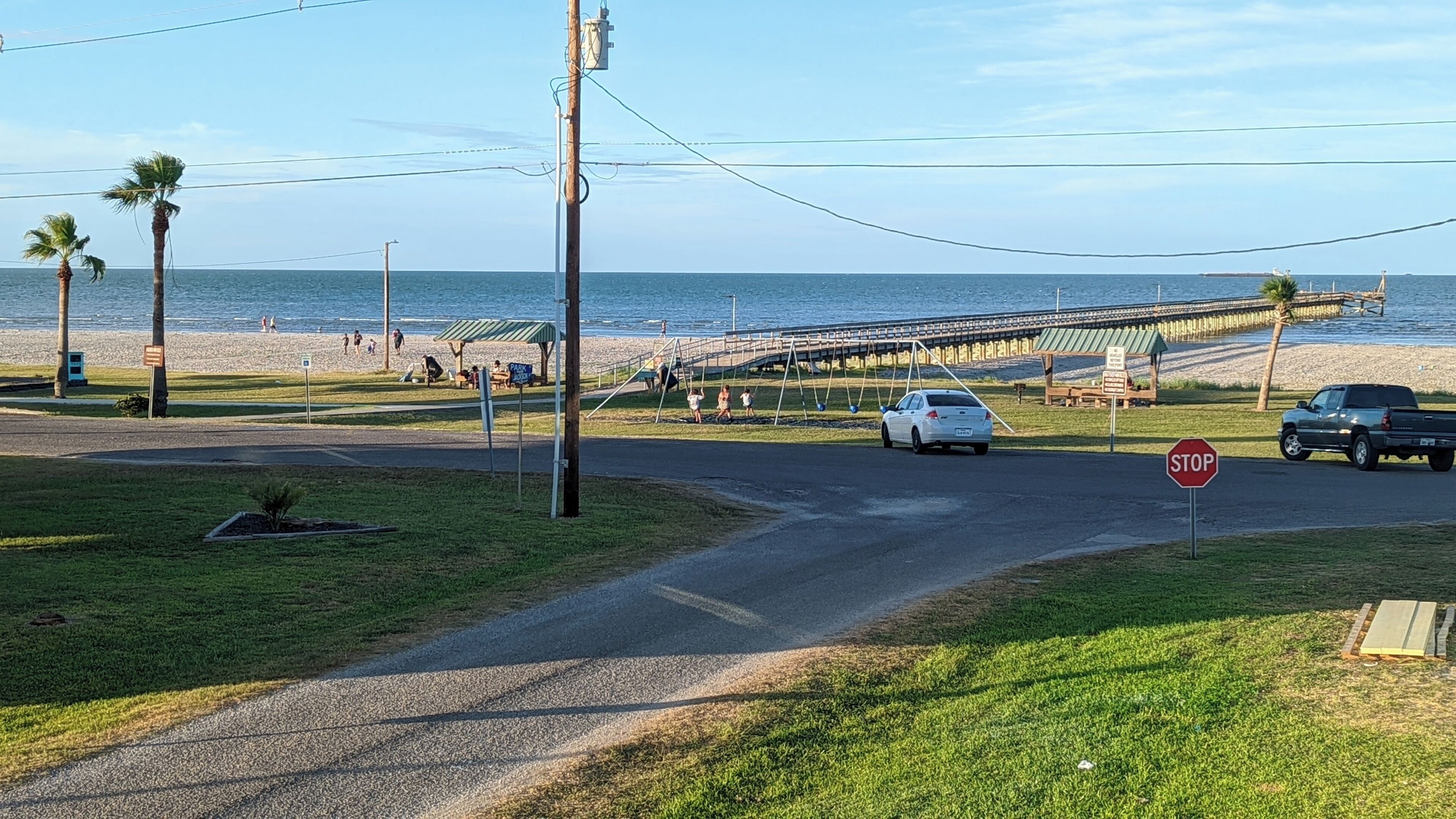 Eine Küstenstraße mit einem Stoppschild, einer Fußgängerbrücke und einem Strand im Hintergrund.