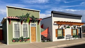 Two small, single-story buildings with green and white exteriors, wooden shutters, and potted plants. - Charming Boutique Hotel with Private Hot Tub
 (De Beque)