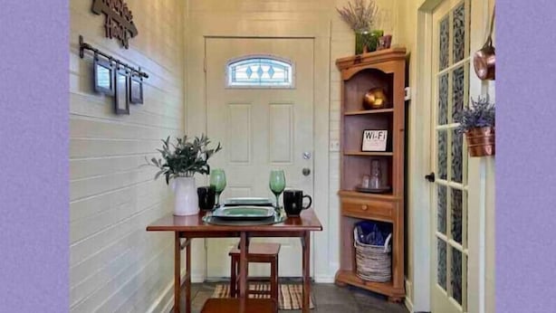 A narrow hallway with a wooden table and chairs, a chandelier, a door with a stained glass window, and a bookshelf with various items. - Charming Boutique Hotel with Private Hot Tub
 (De Beque)