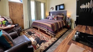 A bedroom with a large bed, a TV, a wooden door, and a dining area with a table and chairs. - Charming Boutique Hotel with Private Hot Tub
 (De Beque)