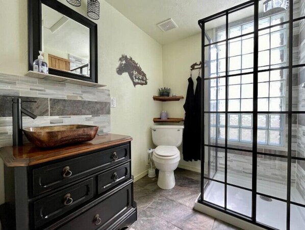 A bathroom with a wooden vanity, a large mirror, a horse decal, a toilet, and a window with a grid pattern.