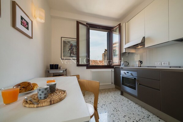 A modern kitchen with white cabinets, a dining table with breakfast items, and a view through an open window.