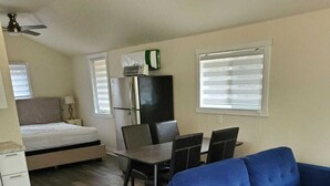 En kompakt opholdsstue med seng, blå sofa, spisebord med stole og et lille tekøkken.