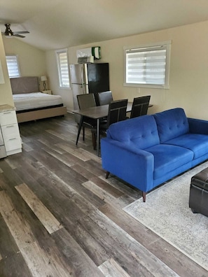 A compact living space with a bed, a blue sofa, a dining table with chairs, and a small kitchenette. - COZY CABIN IN THE WOODS FOR 2. SPACIOUS WELL APPOINTED. NEW LISTING! (Killaloe)