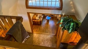 Un espace de vie de style loft avec un escalier en bois, un coin salon confortable doté d’un canapé en cuir et une grande fenêtre en arc de cercle donnant sur un jardin.