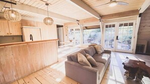 A wooden interior with a sofa, ceiling fan, and large windows. - Clarity Cabin A-Frame Sanctuary w Hot Tub, Fireplace, Grill, AC, Hammock Chairs, Fire Pit, Pets OK (Idyllwild-Pine Cove)