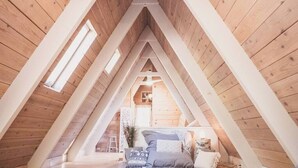 An attic bedroom with wooden beams, a bed, and a window. - Clarity Cabin A-Frame Sanctuary w Hot Tub, Fireplace, Grill, AC, Hammock Chairs, Fire Pit, Pets OK (Idyllwild-Pine Cove)