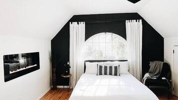 Ein Schlafzimmer mit einem großen Bett, einem Deckenventilator, einem Fenster mit Vorhängen und einem Wandbild.