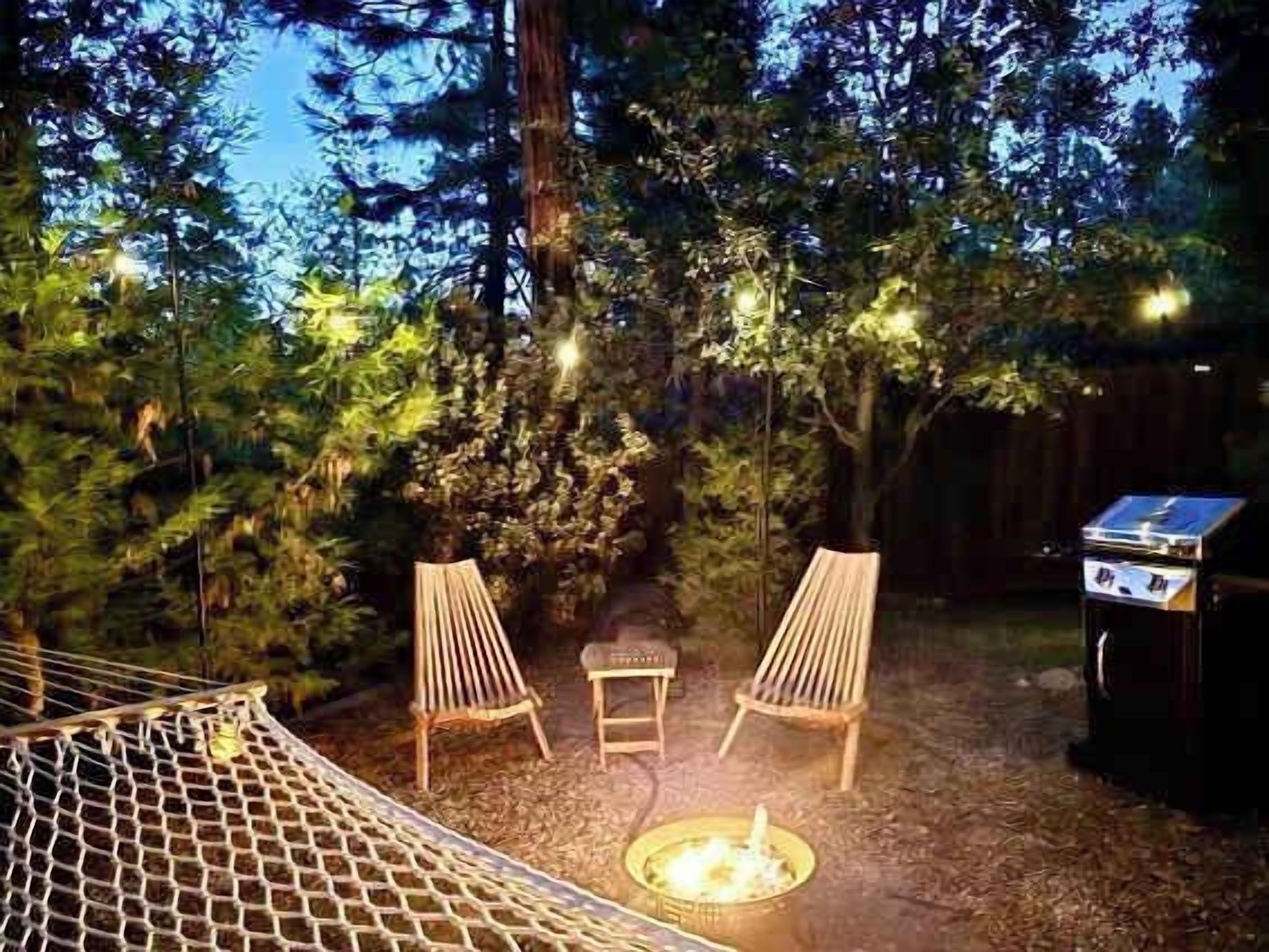Un hamac, deux chaises, une petite table et un barbecue dans un jardin avec des arbres et une clôture.