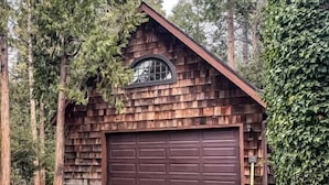 A rustic cabin with a stone-paved driveway, a large garage door, and a wooden shingle exterior.