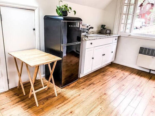 A compact kitchen with a black refrigerator, white cabinets, a wooden table, and a window with a view of a red building.