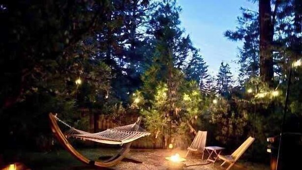 A hammock and two chairs set up in a forested area with string lights.