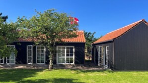 Een gebouw met twee verdiepingen, een rode pannendak, grote ramen en een verzorgd gazon.