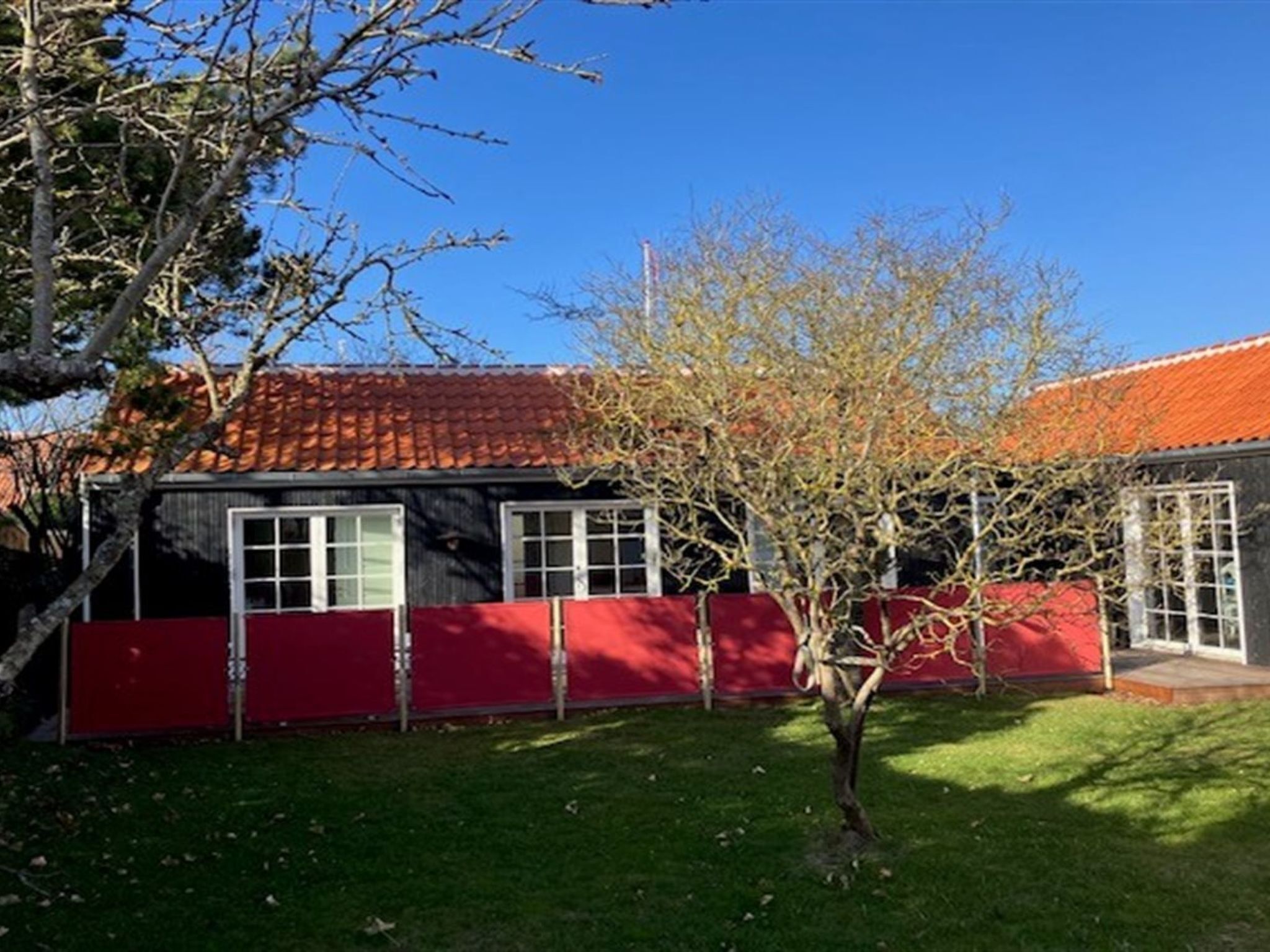 A house with a red fence, a tree in front, and a red-tiled roof.