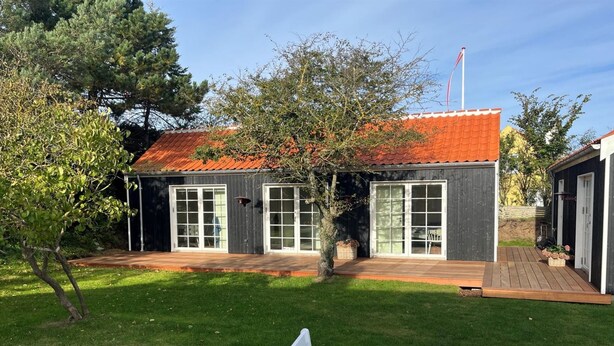 Een gebouw met twee verdiepingen, een rode pannendak, grote ramen en een terras.