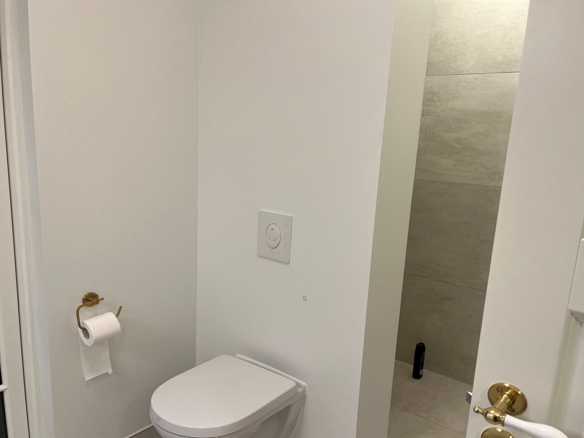 Un bagno piccolo e bianco con il water, un rotolo di carta igienica e una zona doccia.
