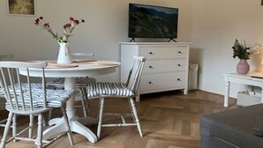 Een eethoek met een ronde tafel, gestreepte stoelen, een witte kast en een televisie op een standaard.