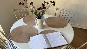 Een ronde eettafel met vier gevlochten placemats, een witte vaas met bloemen en een open menubestand.
